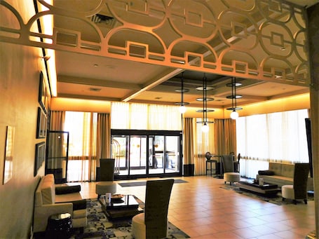 A spacious lobby with a modern design, featuring a seating area with sofas and armchairs, a coffee table, and a patterned rug.