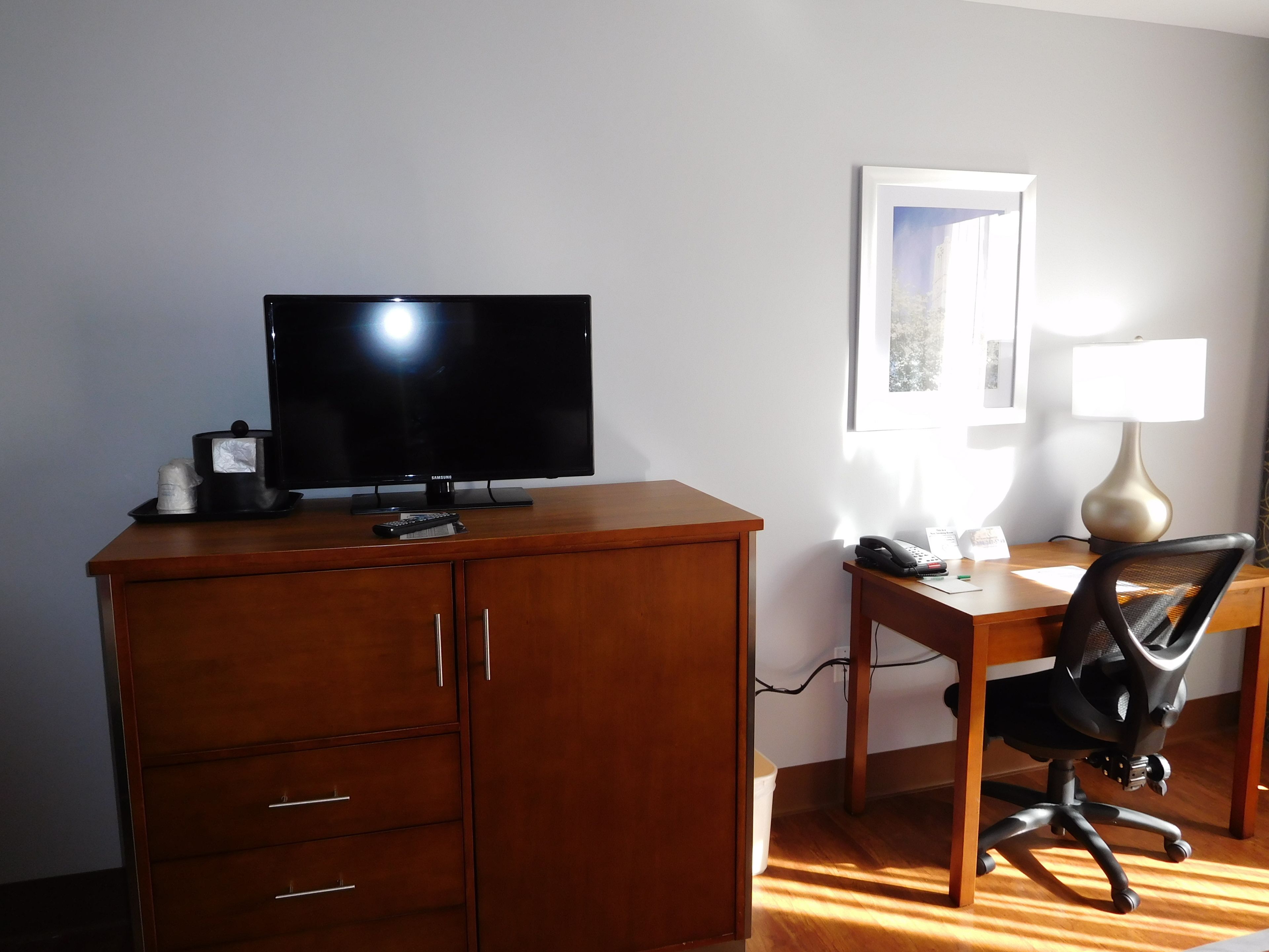 Una habitación con un escritorio de madera, una silla de oficina negra, un televisor y una lámpara.
