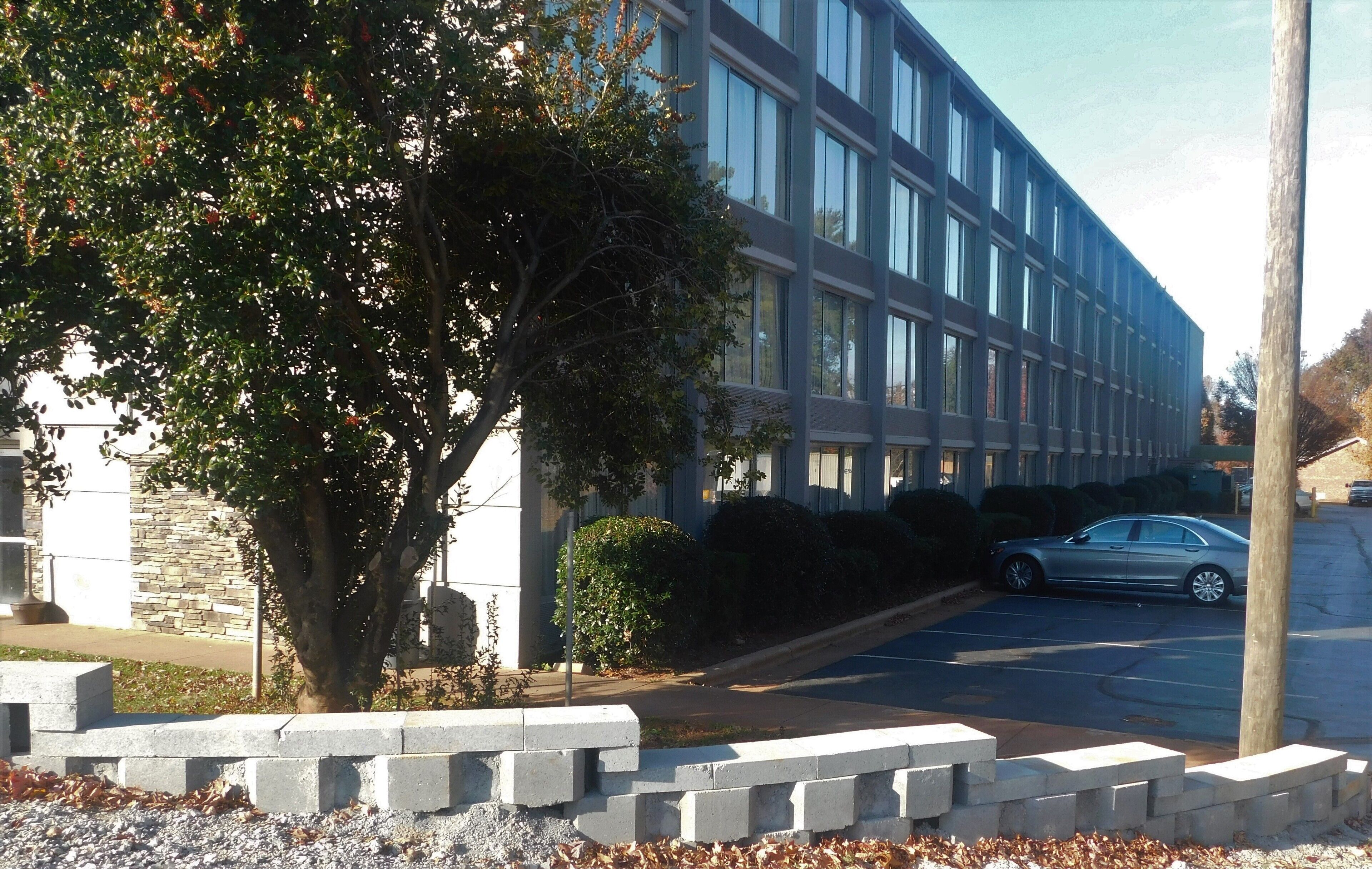 Un edificio moderno con estacionamiento, un árbol y un coche.