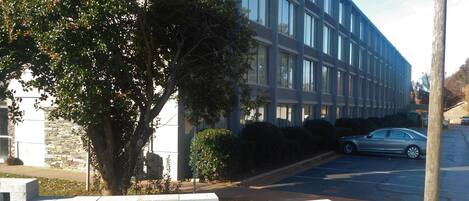 Un edificio moderno con estacionamiento, un árbol y un coche.