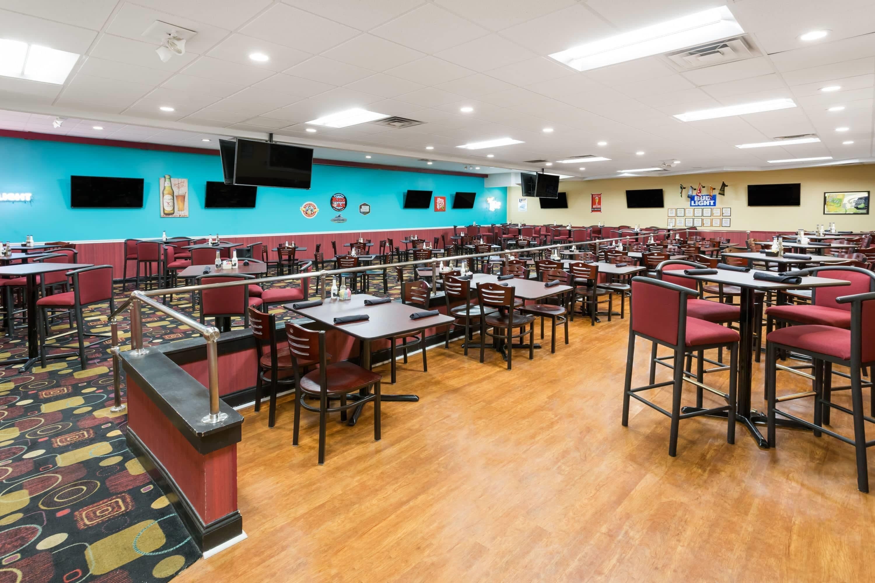 A large dining area with multiple tables and chairs, a stage, and a blue wall with mounted screens.