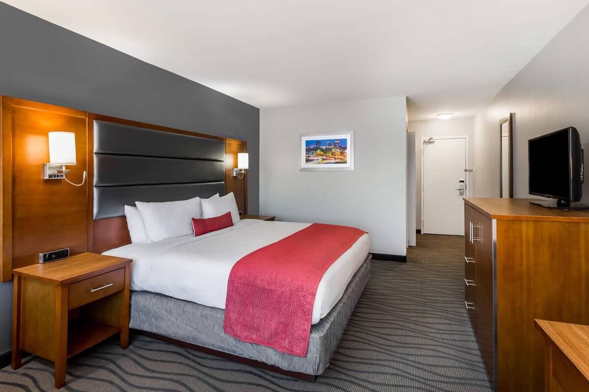 Ein Hotelzimmer mit Bett, Nachttisch, Fernseher und Blick auf die Stadt.