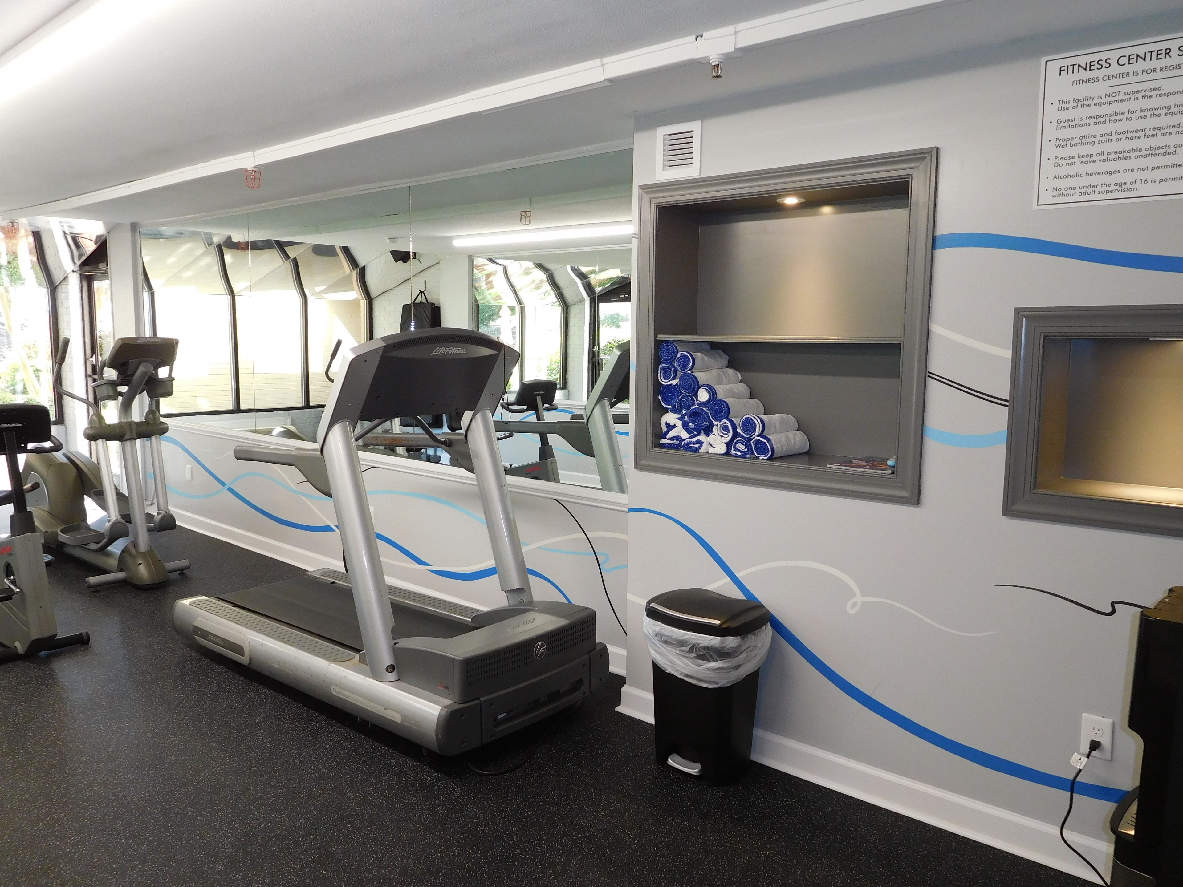 A fitness center with treadmills, exercise equipment, and a wall-mounted shelf with towels.