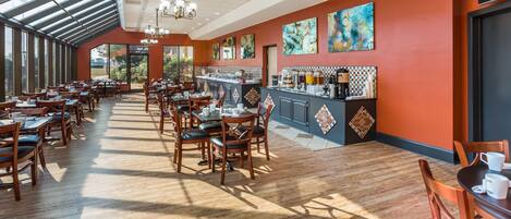 A spacious restaurant with high ceilings, large windows, and a long counter with a coffee station.