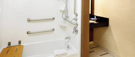 A modern bathroom with a bathtub, grab bars, a wooden bath mat, and a sink with a black countertop.