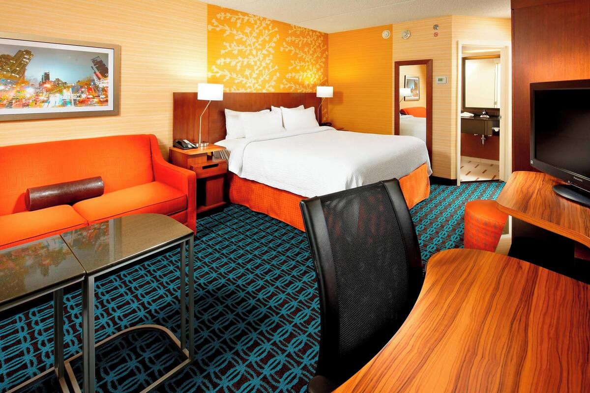 Une chambre d’hôtel avec un lit, un canapé, un bureau, une télévision et une salle de bain visible à travers une porte ouverte.