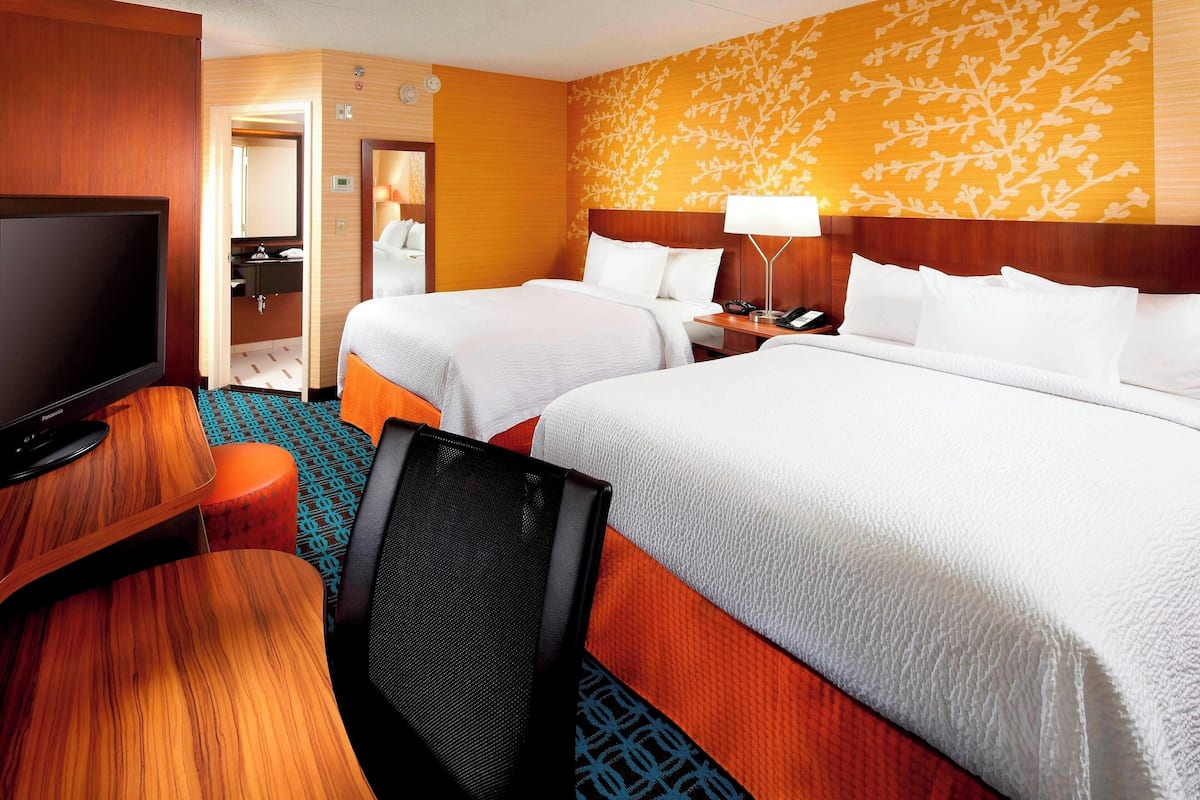 Une chambre d’hôtel avec deux lits, une télévision, un bureau et une salle de bain visible à travers une porte ouverte.
