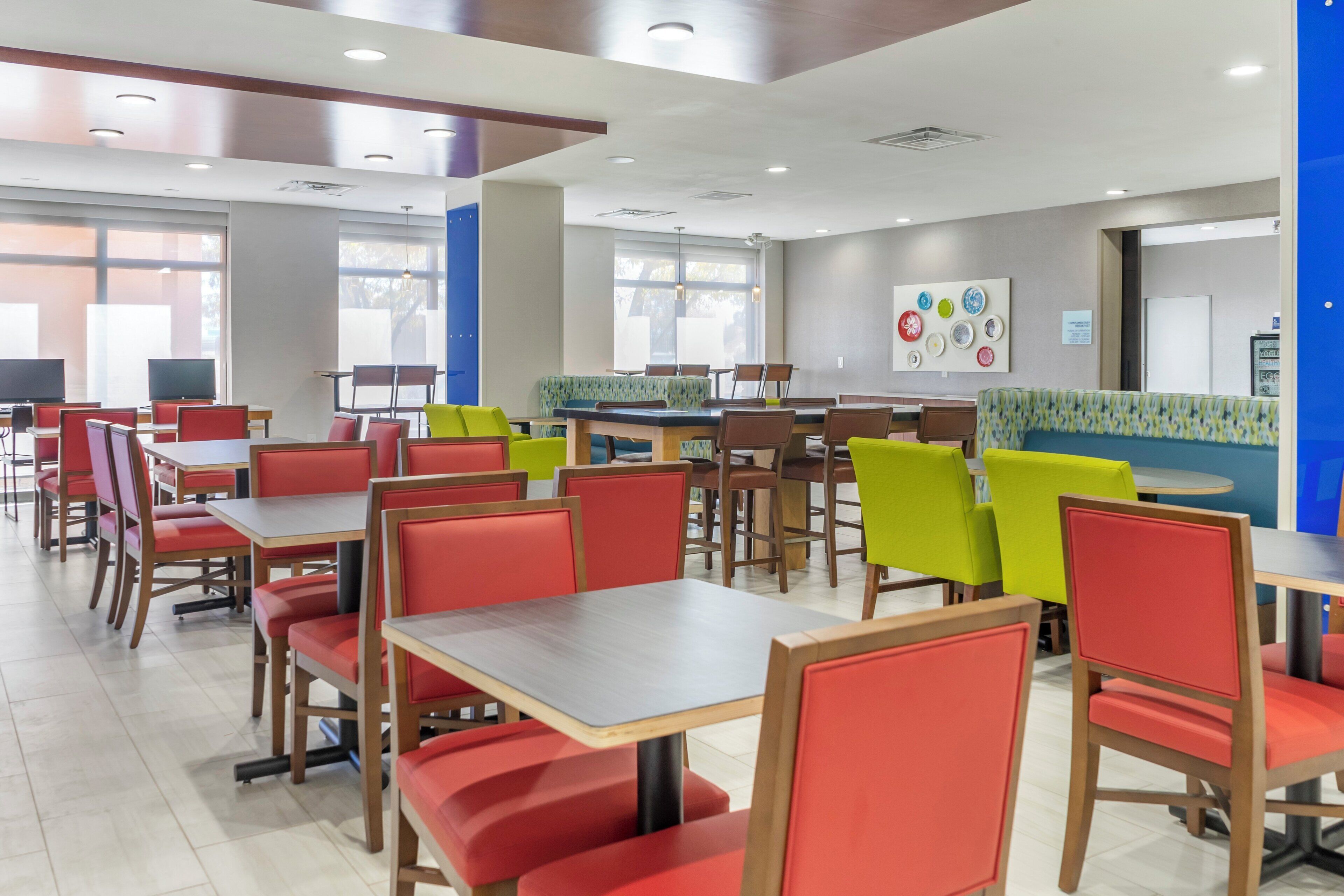 A cafeteria with multiple tables and chairs, some with red cushions, and a blue counter area.
