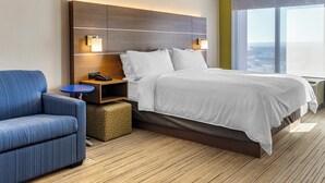 Ein modernes Hotelzimmer mit einem großen Bett, einem blauen Sessel, einem kleinen runden Tisch und einem Nachttisch.