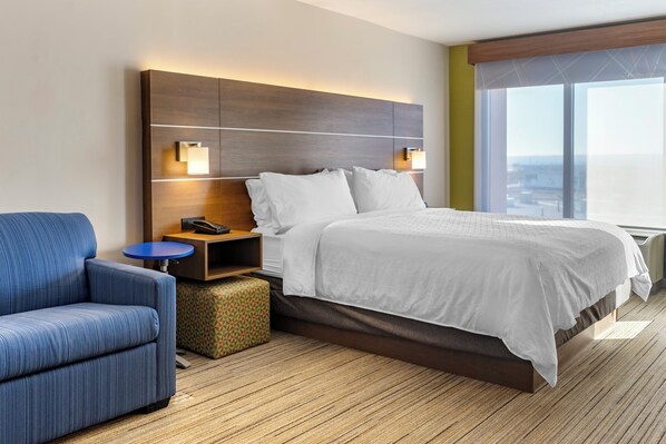 Een moderne hotelkamer met een groot bed, een blauwe fauteuil, een klein rond tafeltje en een nachtkastje.