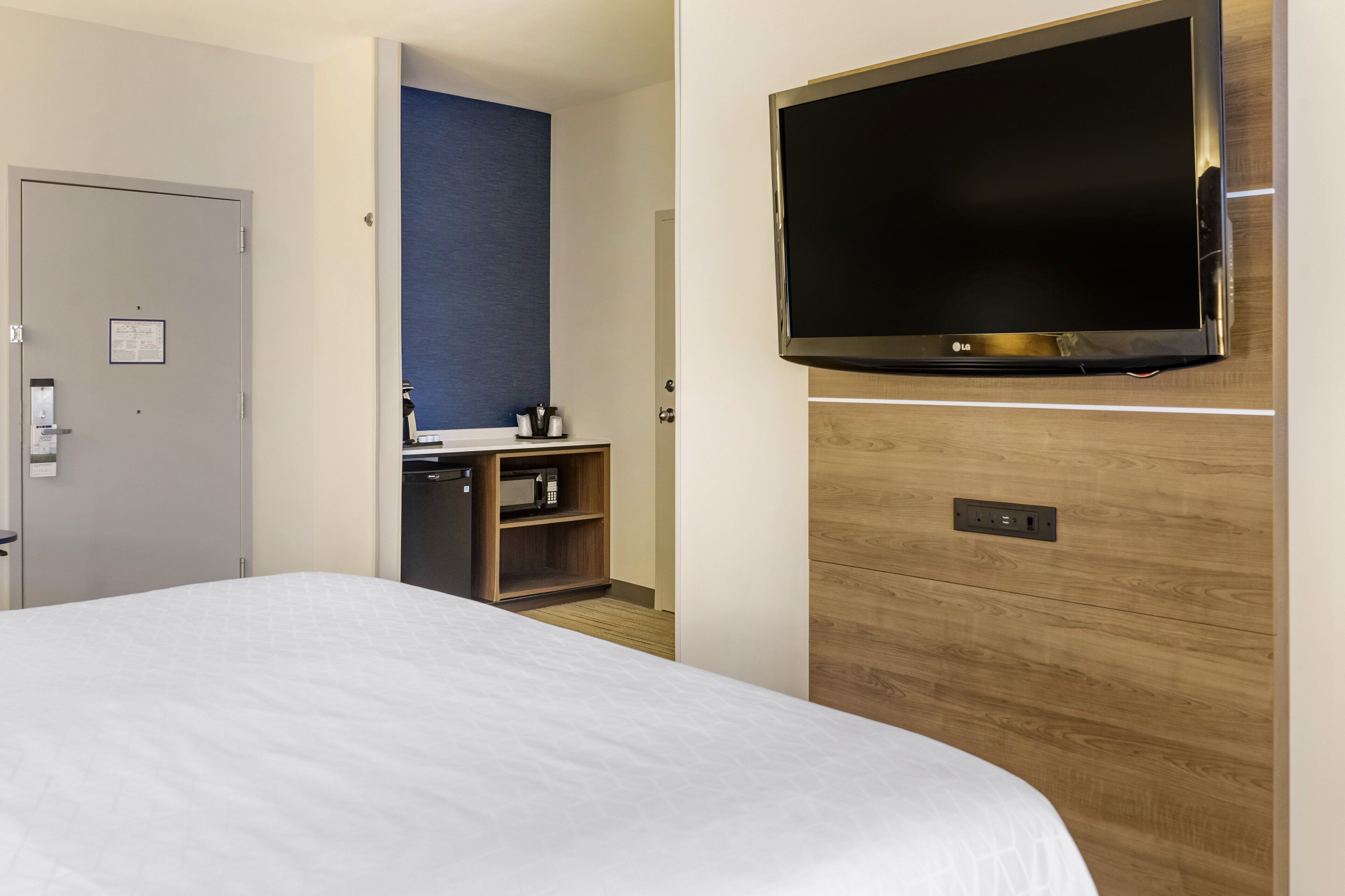 A hotel room with a large bed, a TV mounted on the wall, a wooden cabinet, and a door.
