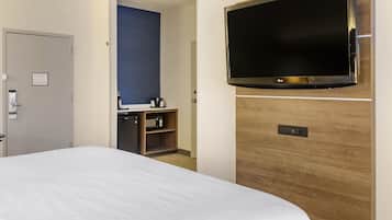 A hotel room with a large bed, a TV mounted on the wall, a wooden cabinet, and a door.