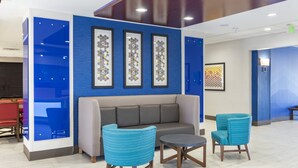 Eine moderne Lobby mit blauer Akzentwand, einem grauen Sofa, zwei blauen Sesseln und einem kleinen runden Tisch.