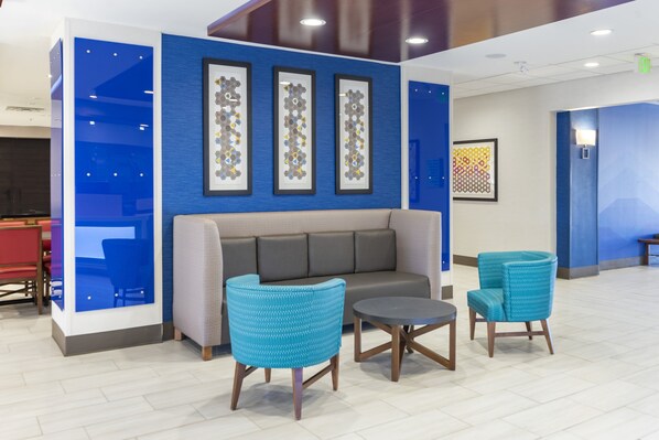 A modern lobby with a blue accent wall, a grey sofa, two blue armchairs, and a small round table. - Holiday Inn Express Hotel & Suites Albuquerque Midtown by IHG (Albuquerque)