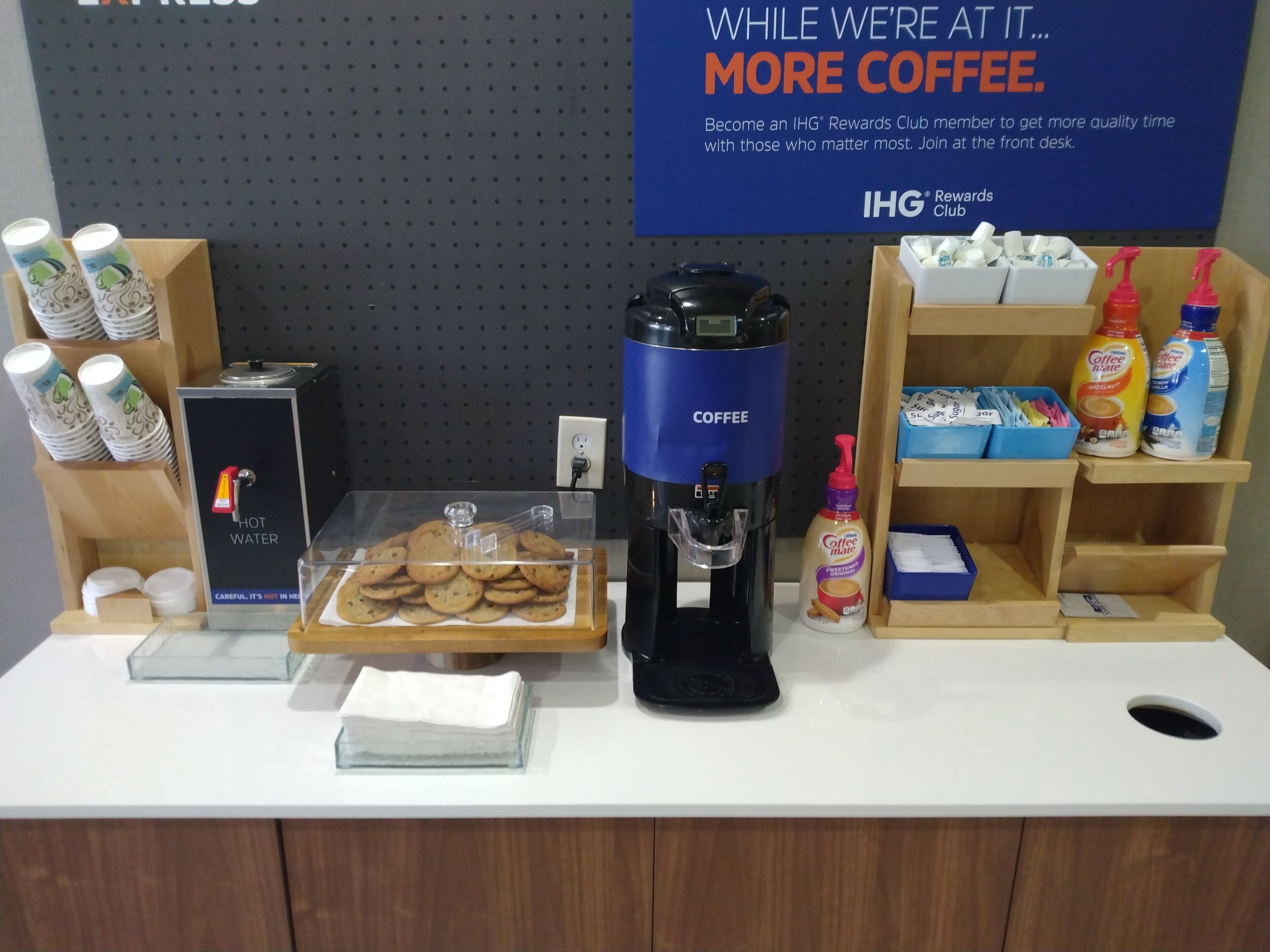 Een koffiehoek met een koffieapparaat, een heetwaterdispenser en een schotel met koekjes.