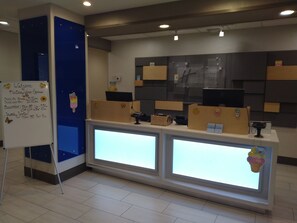 A reception desk with a whiteboard displaying check-in and shuttle service times, a blue wall, and a modern design with recessed lighting. - Holiday Inn Express Hotel & Suites Albuquerque Midtown by IHG (Albuquerque)