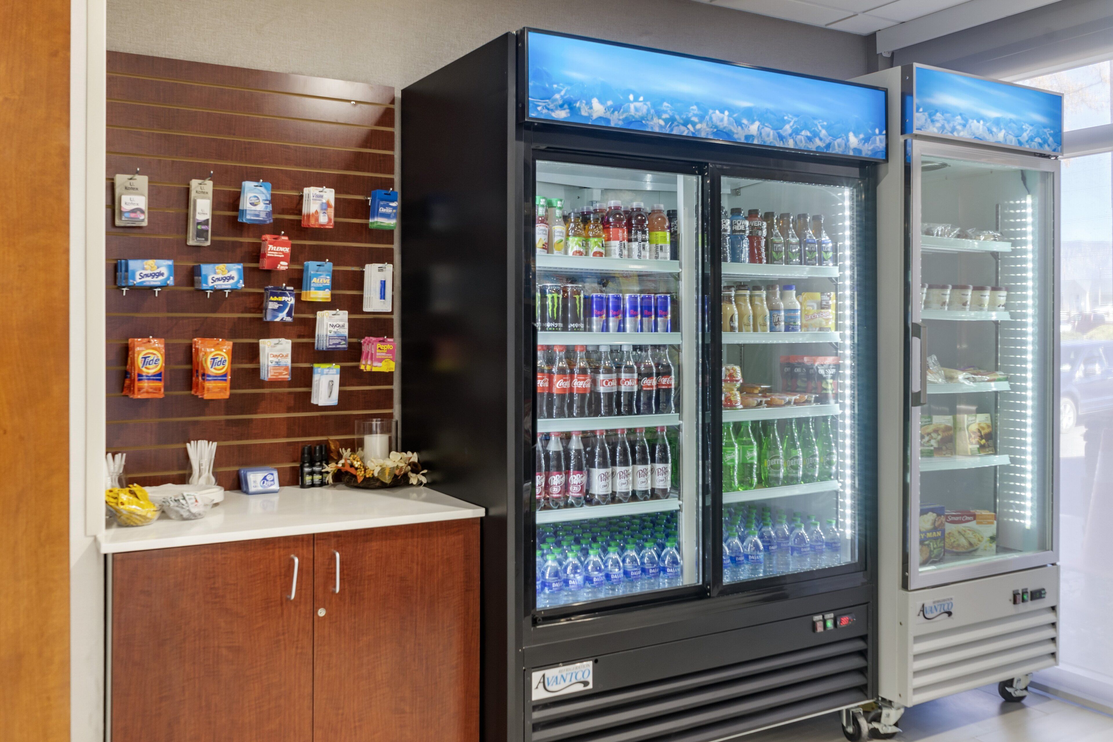 A vending machine with various beverages and snacks, a wooden counter with packaged goods, and a refrigerated display case with bottled drinks.