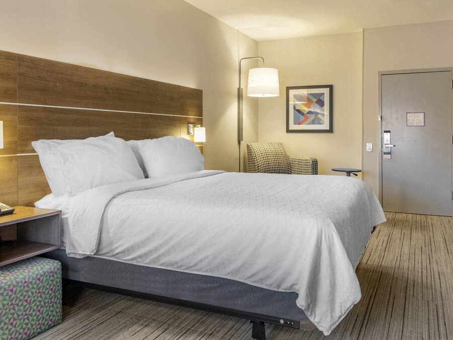 A hotel room with a bed, bedside lamps, a chair, a desk, and a door.