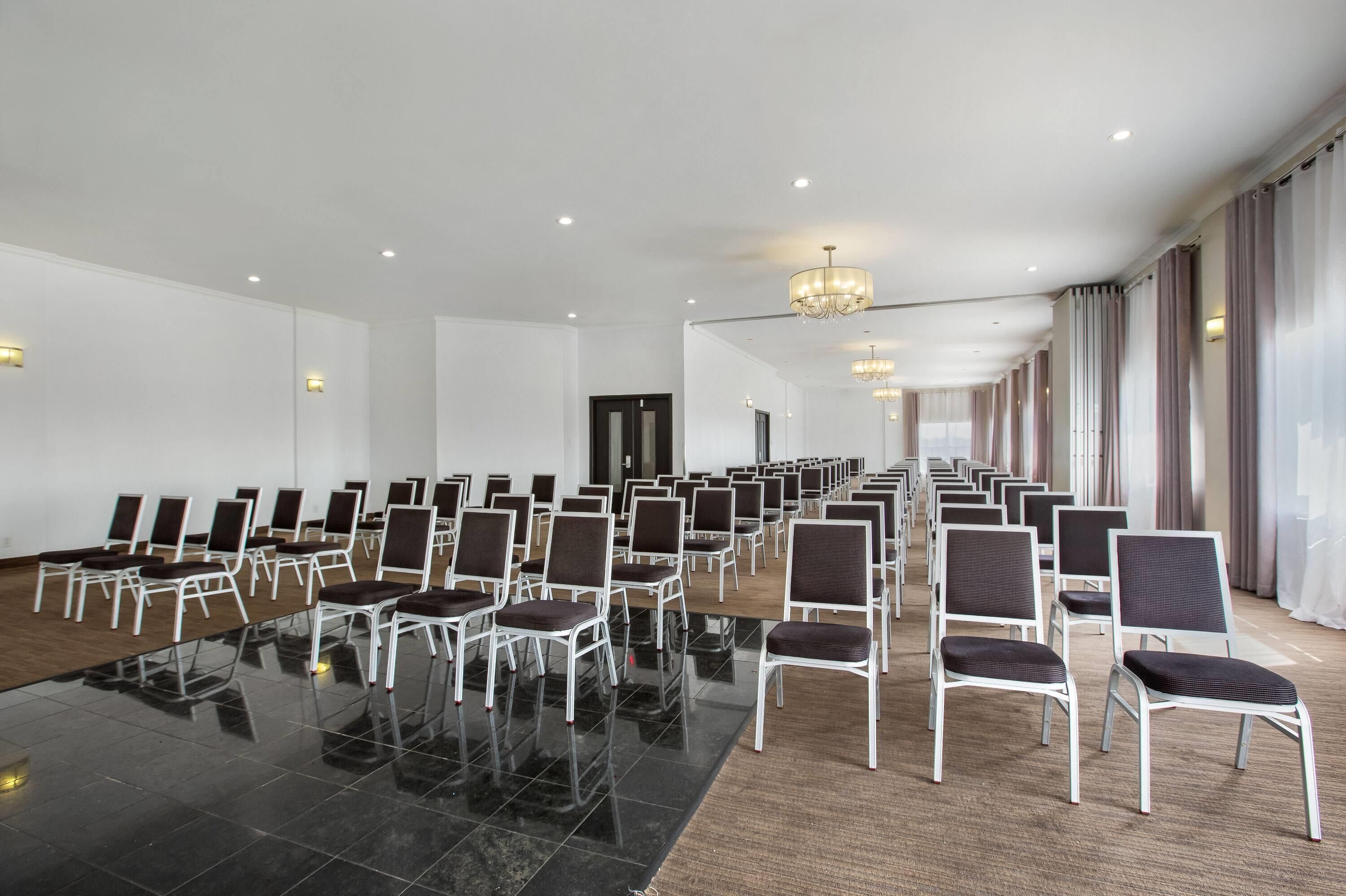 Une grande salle de conférence avec des rangées de chaises, une table en verre et un lustre.