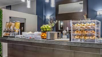 Una barra de desayuno con una variedad de alimentos, como frutas, pasteles y una máquina de café.