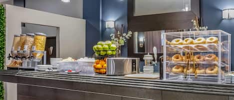 A breakfast bar with a variety of food items, including fruits, pastries, and a coffee machine.
