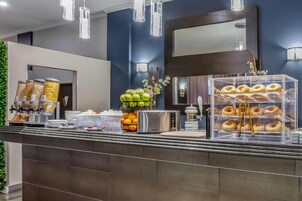 Una barra de desayuno con una variedad de alimentos, como frutas, pasteles y una máquina de café.