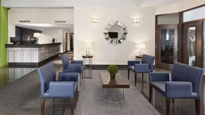 Un vestíbulo con mostrador de recepción, sillas azules, una mesa de centro con planta y un espejo grande en la pared.