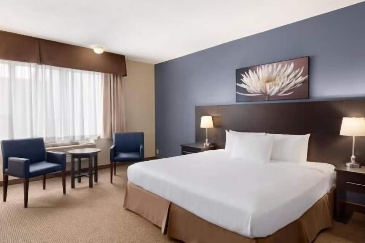 Een hotelkamer met een groot bed, twee nachtkastjes met lampen, een bureau met stoel en een raam met gordijnen.