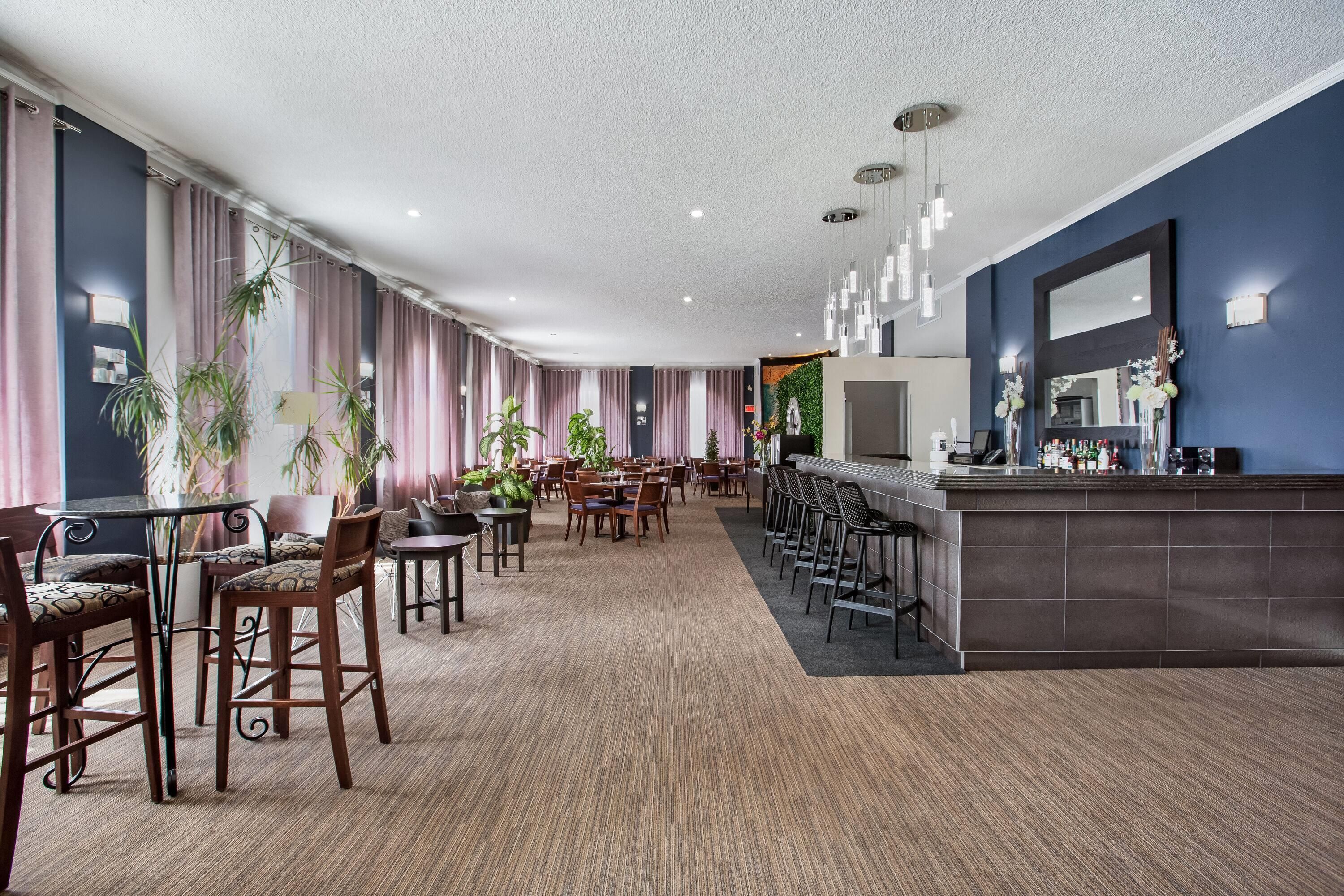 Un hall d’hôtel doté d’un long comptoir d’accueil, de plusieurs espaces aménagés avec des fauteuils et des tables, et d’un grand miroir au-dessus du comptoir.