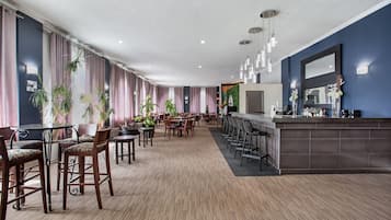 Un hall d’hôtel doté d’un long comptoir d’accueil, de plusieurs espaces aménagés avec des fauteuils et des tables, et d’un grand miroir au-dessus du comptoir.