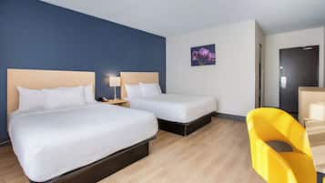 Habitación de hotel con dos camas, un escritorio, una silla, una mesita de noche y una lámpara de pared.