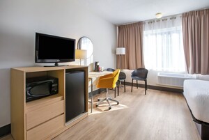 Une chambre d’hôtel équipée d’un téléviseur à écran plat, d’un bureau avec une lampe, d’une chaise, d’un lit et d’une fenêtre avec des rideaux.