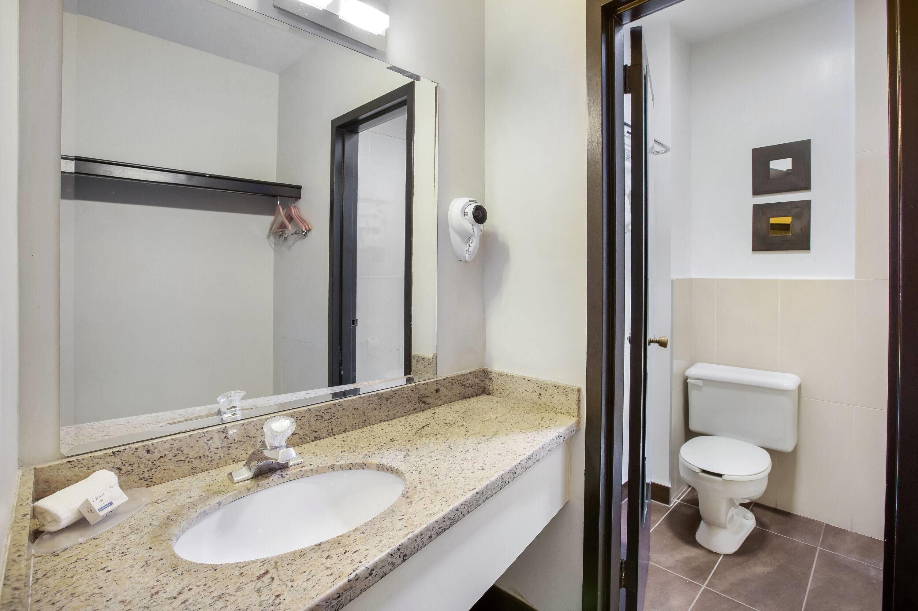 Baño con lavamanos, espejo, inodoro y una cámara de seguridad.