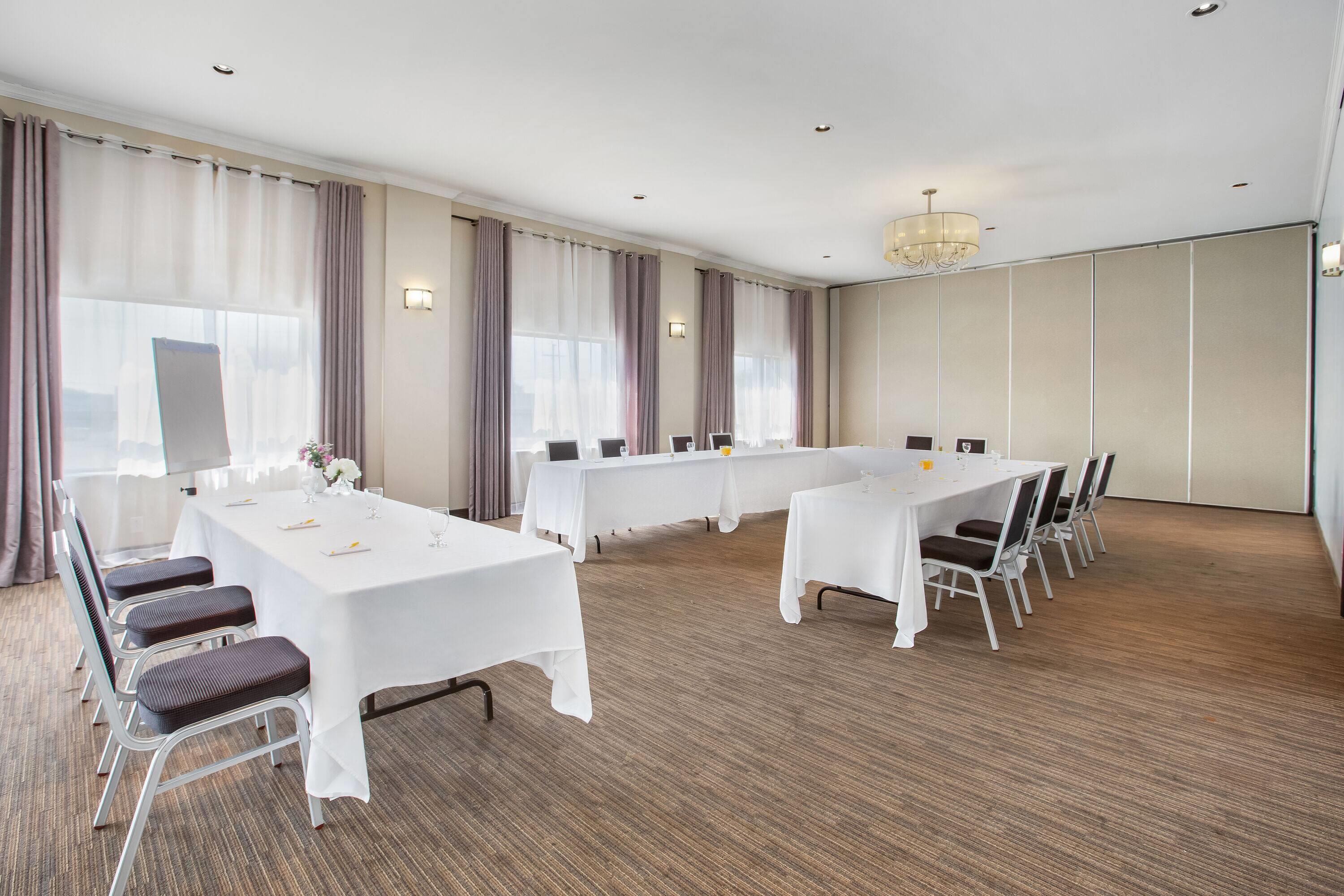 A conference room with multiple tables and chairs, large windows with curtains, and a chandelier.