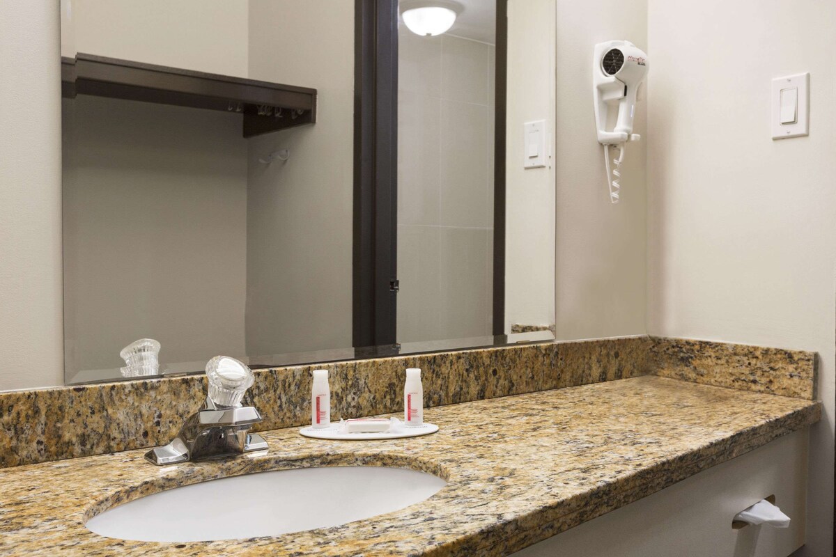A bathroom with a granite countertop, a sink, a mirror, a hairdryer, and a towel dispenser.
