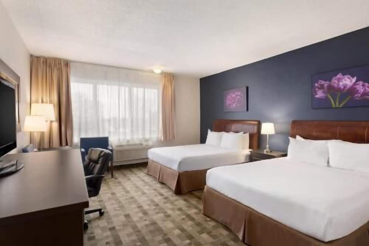 Een hotelkamer met twee bedden, een bureau, een stoel, een televisie en een raam met gordijnen.