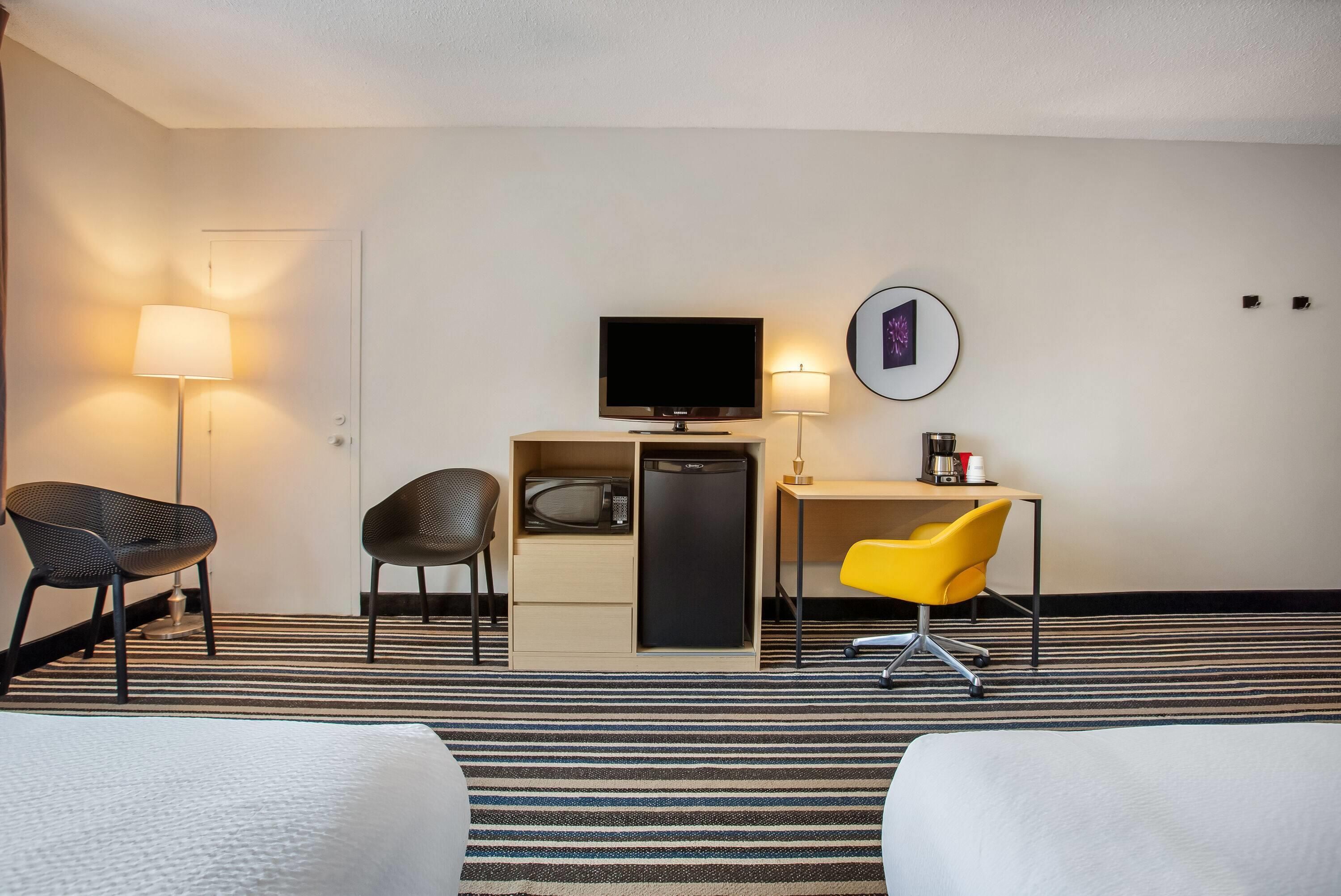 A hotel room with a bed, a desk with a computer, a television, and two chairs.