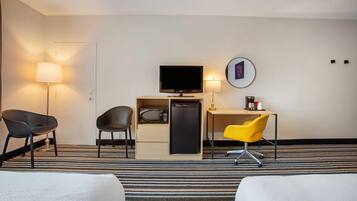 A hotel room with a bed, a desk with a computer, a television, and two chairs.