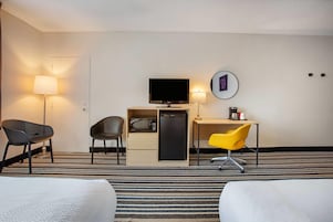 A hotel room with a bed, a desk with a computer, a television, and two chairs.