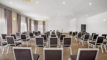 Un salón de conferencias con filas de sillas, una lámpara de araña y un amplio ventanal con cortinas.