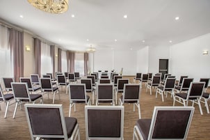 A conference room with rows of chairs, a chandelier, and a large window with curtains.