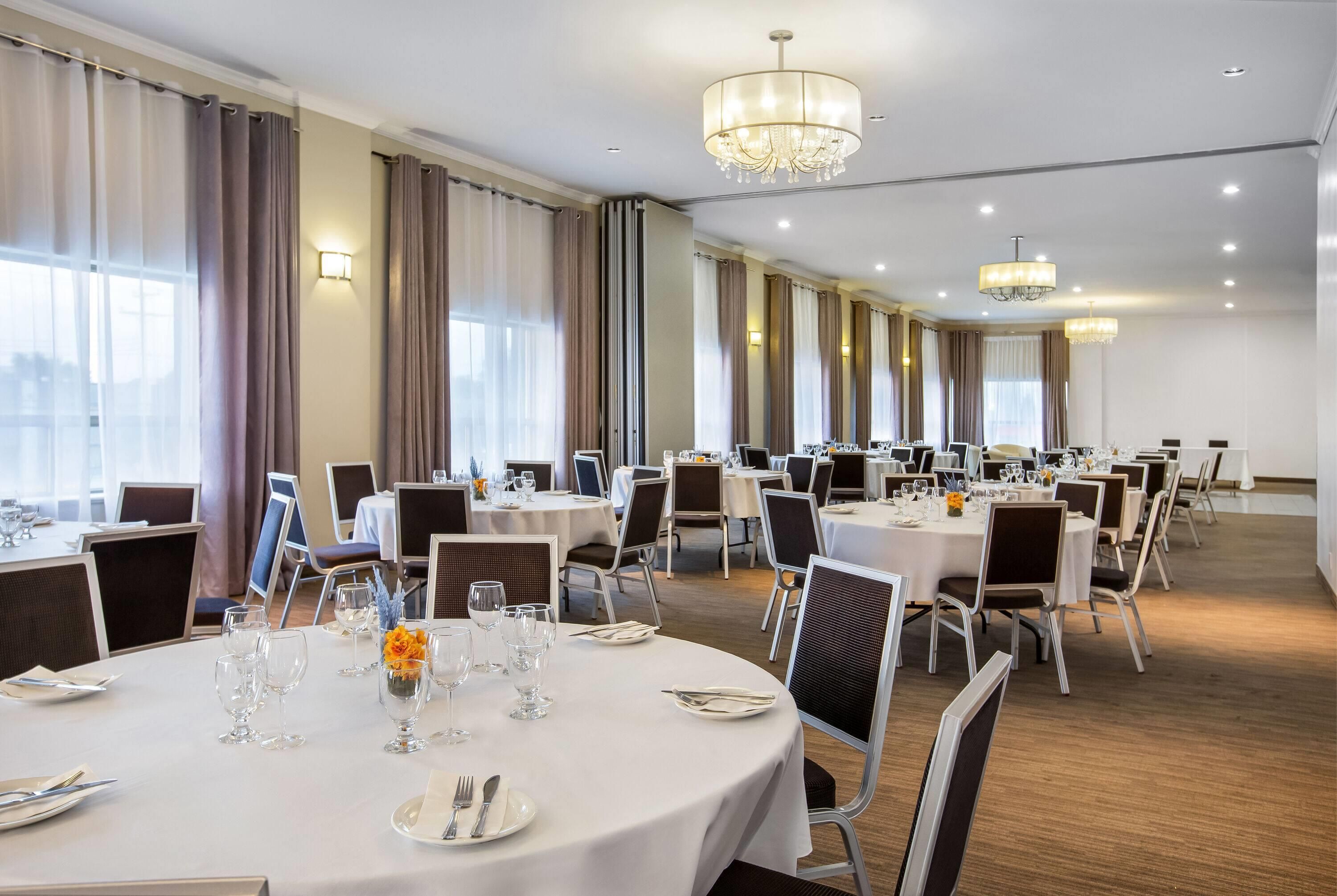 Une salle à manger d’hôtel avec des tables rondes, des chaises et des lustres.