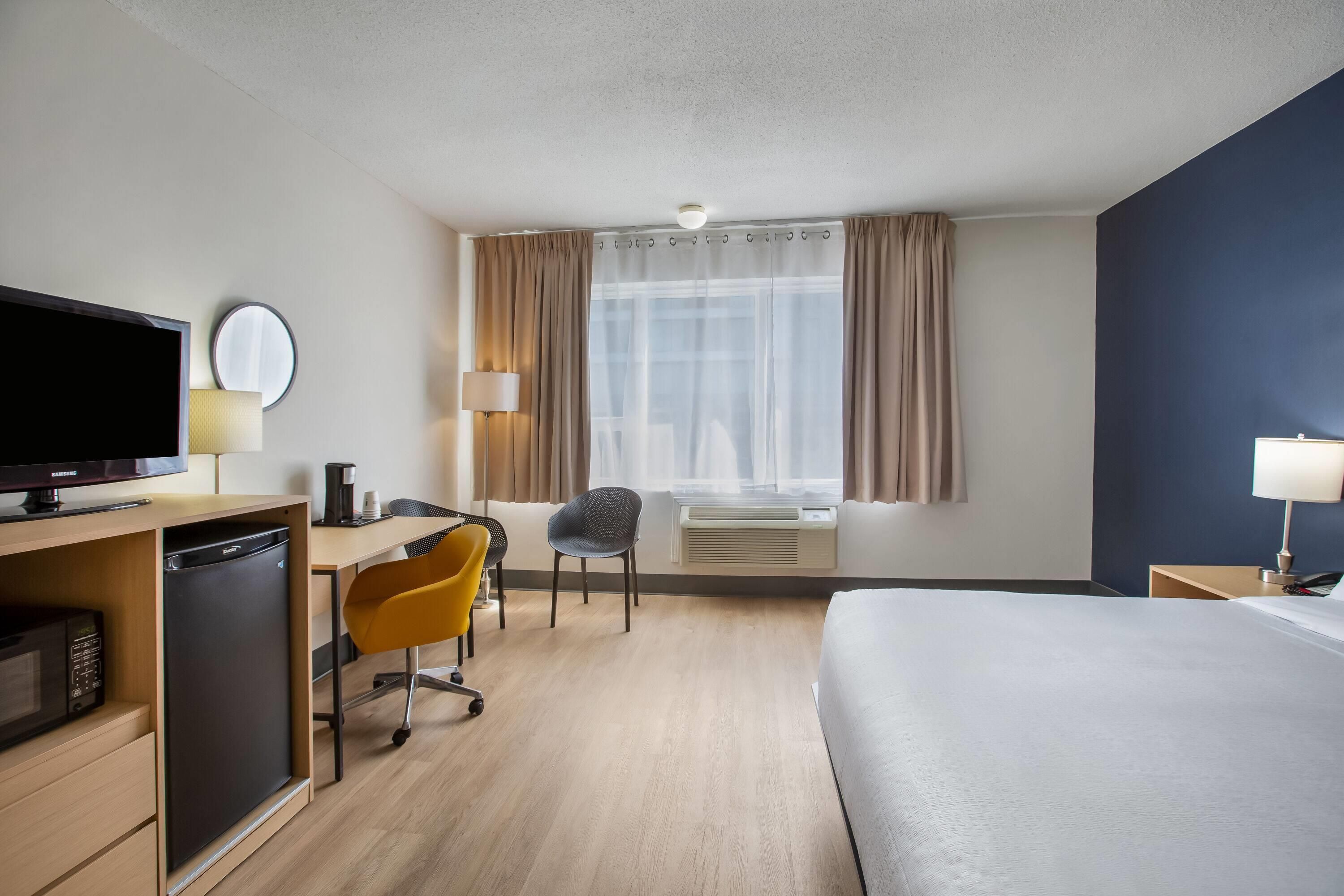 A hotel room with a bed, desk, chair, television, and a window with curtains.