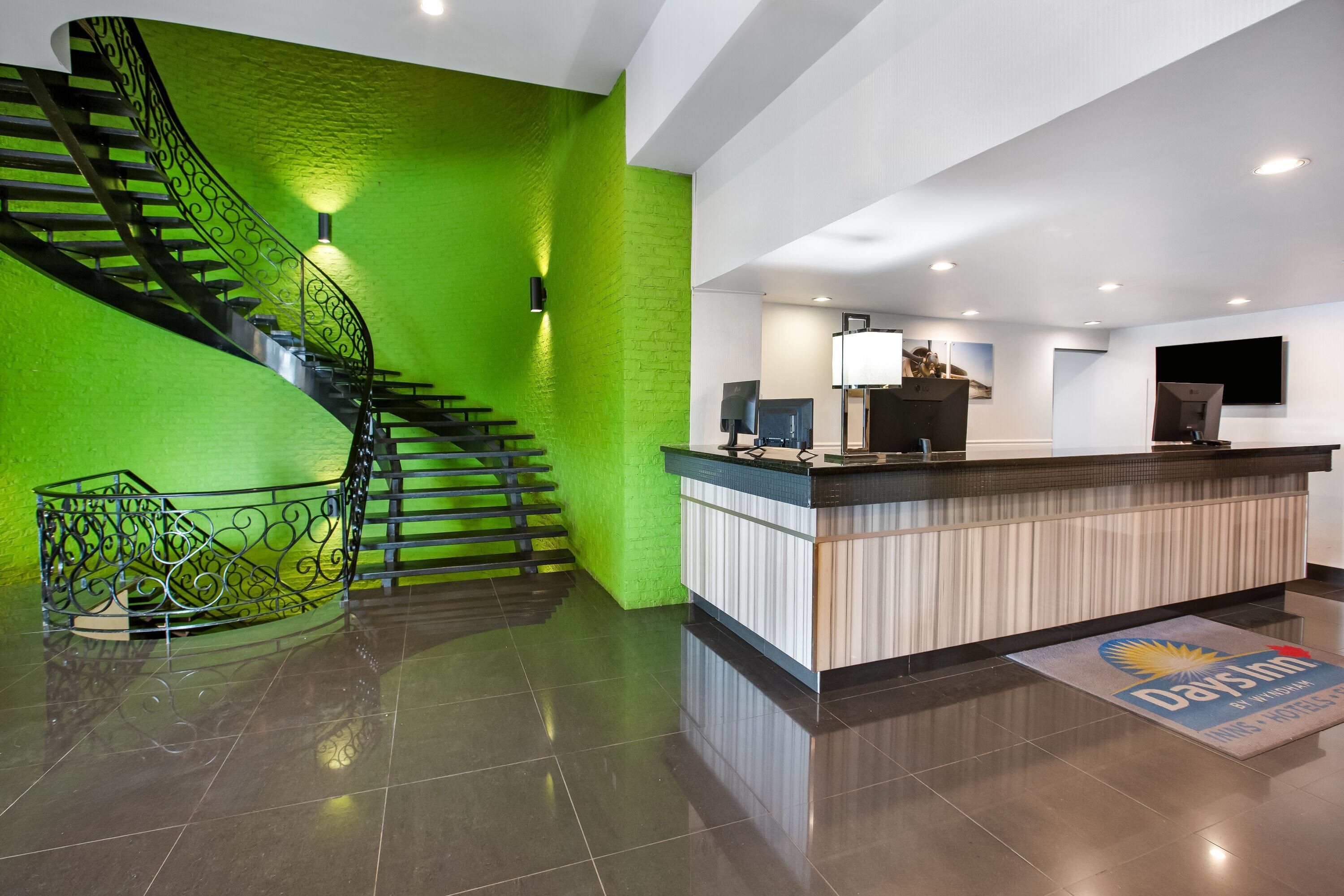 Un hall d’hôtel avec un mur végétal, un escalier, un comptoir d’accueil et un téléviseur à écran plat.