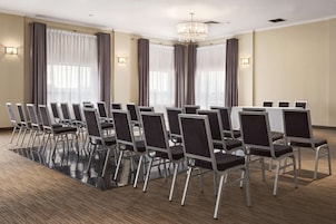 Un salón de conferencias con filas de sillas, ventanas amplias con cortinas y una araña.
