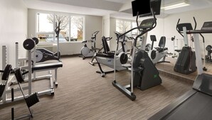 Un gimnasio con diversos equipos de ejercicio, ventanas amplias y un televisor montado en la pared.