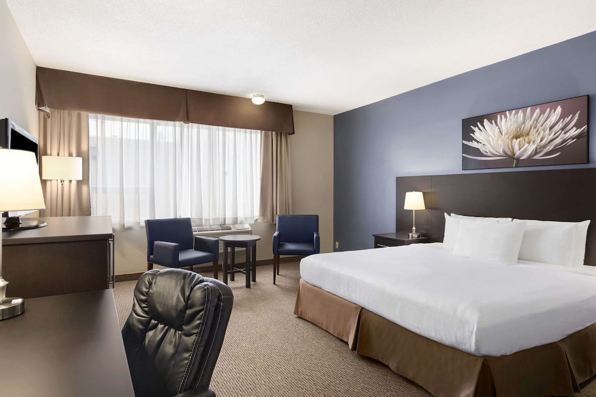 Een hotelkamer met een groot bed, een bureau, twee stoelen, een lamp en een raam met gordijnen.