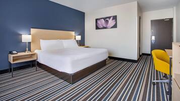 A hotel room with a large bed, a nightstand with a lamp, a desk with a chair, and a door.
