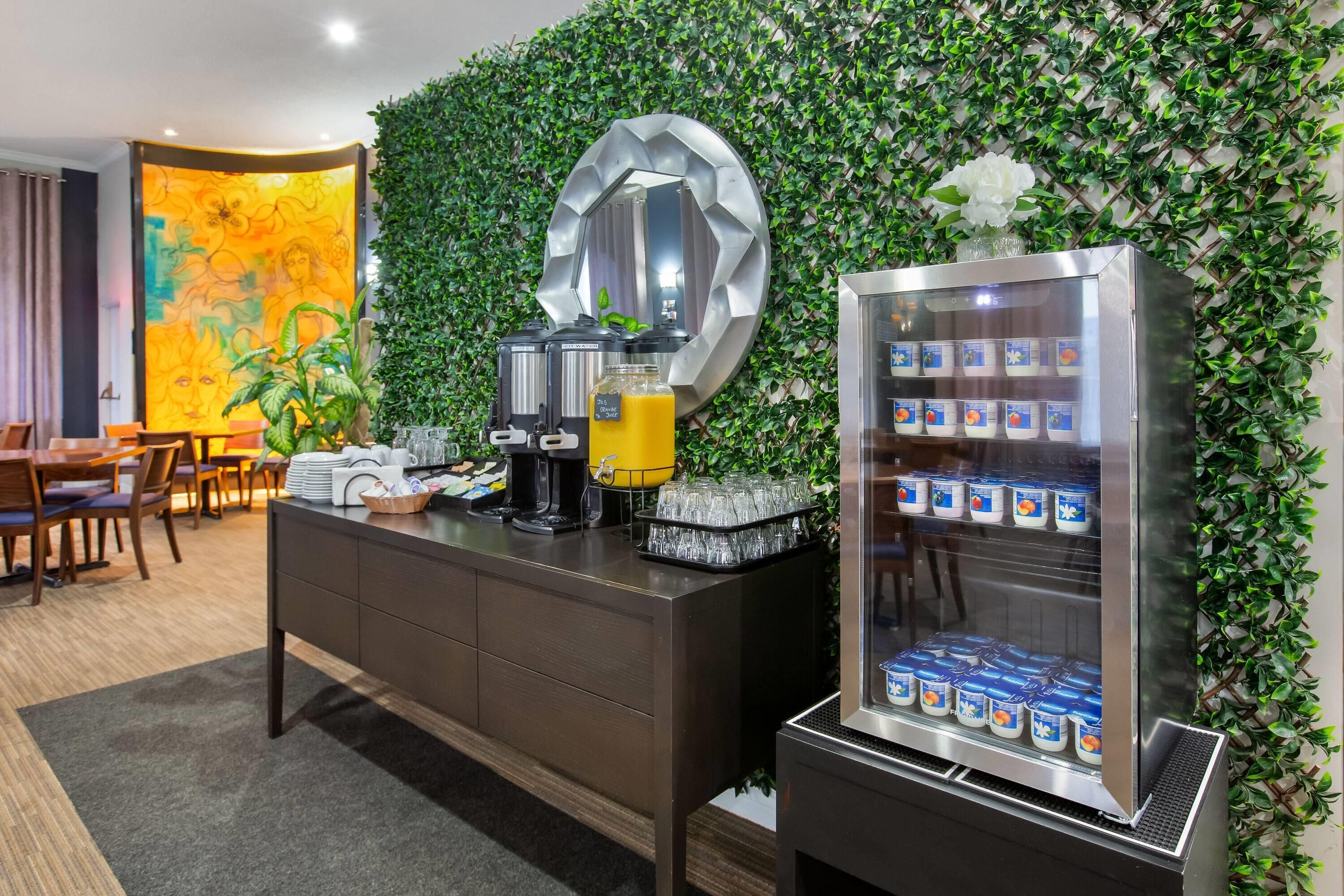 A hotel room with a coffee station, a juice dispenser, and a refrigerator stocked with yogurt.