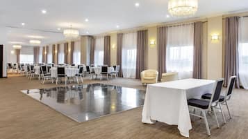 A large conference room with multiple tables and chairs, a central chandelier, and large windows with curtains.